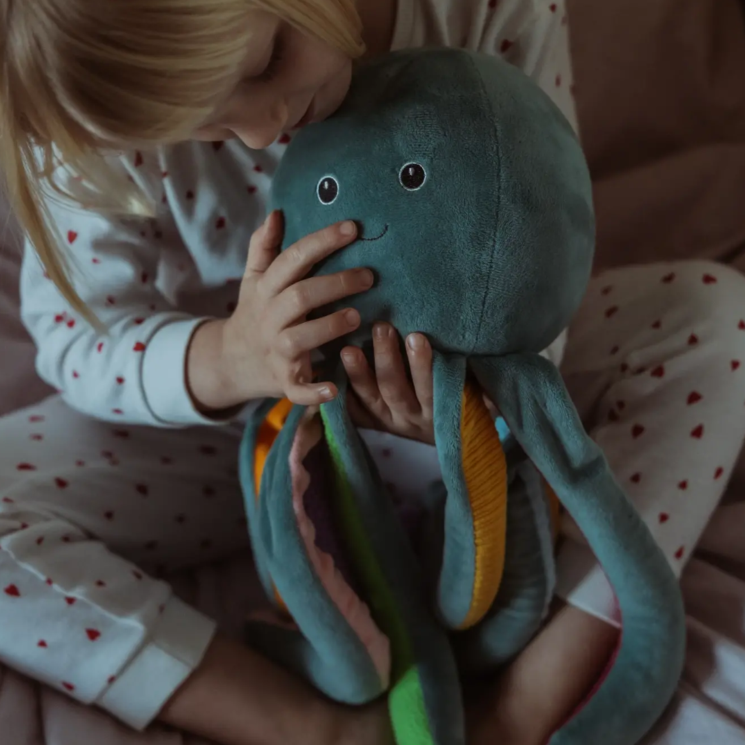 Petrolkleurige ByASTRUP verzwaringsknuffel octopus van 1,2 kg met kleurrijke, getextureerde armen zittend bij een meisje op schoot