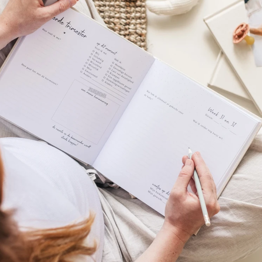 Fyllbooks zwangerschapsdagboek open bij de babychecklist, met babyschoentjes en babykleding ernaast